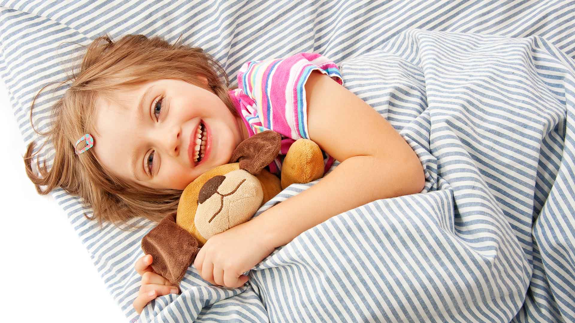 A little girl laying in bed with a teddy bear.