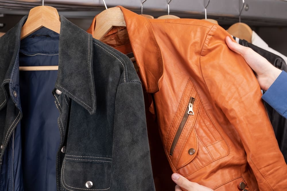 A man is choosing a leather jacket from a rack.
